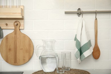 Photo of Jug with water, glasses, towel and utensils in kitchen
