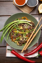 Photo of Stir-fry. Delicious cooked noodles with chicken and vegetables in bowl on wooden table, flat lay