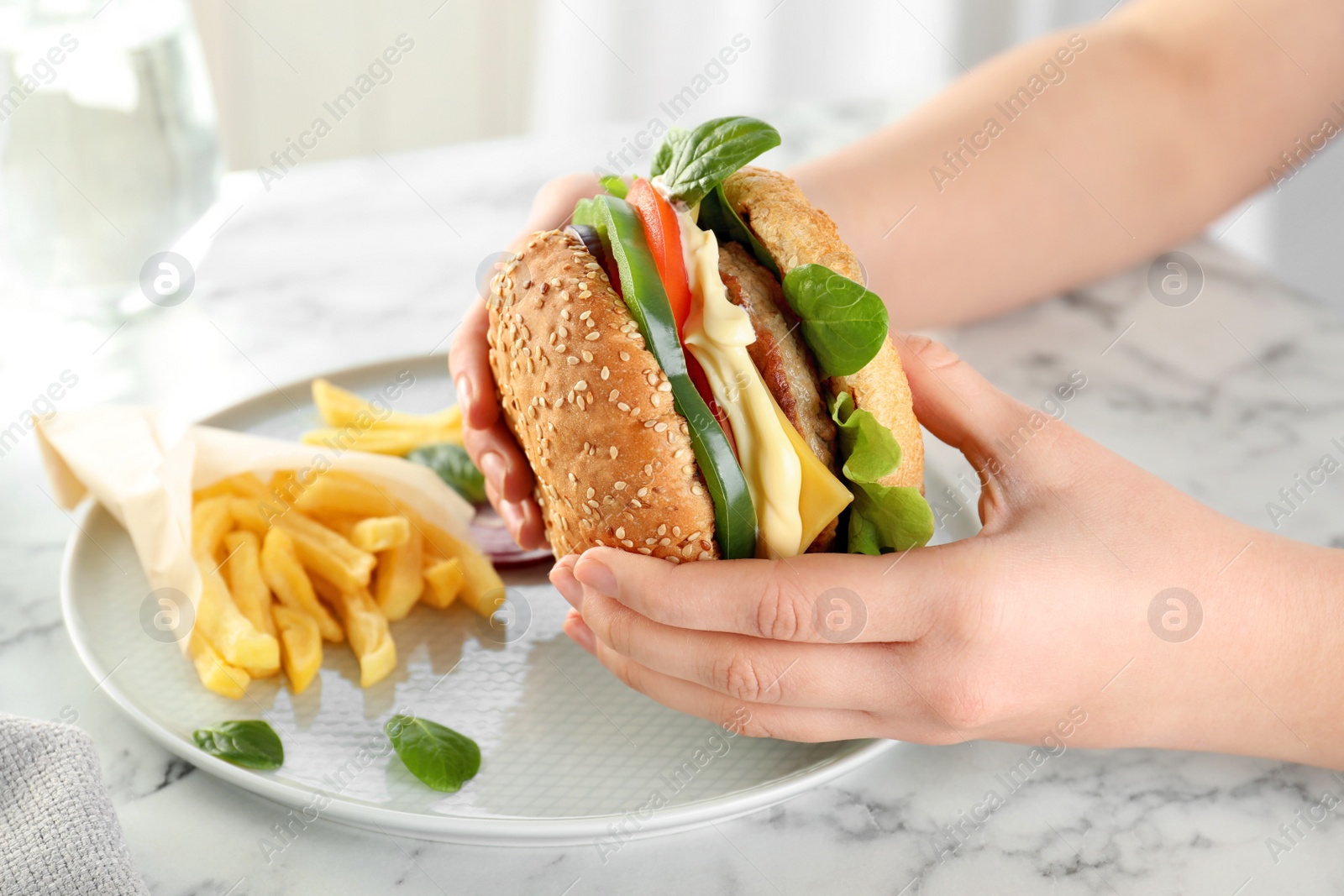 Photo of Woman holding tasty burger over plate at table, closeup