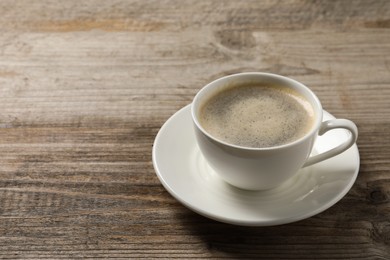 Photo of Tasty coffee in cup on wooden table, closeup. Space for text