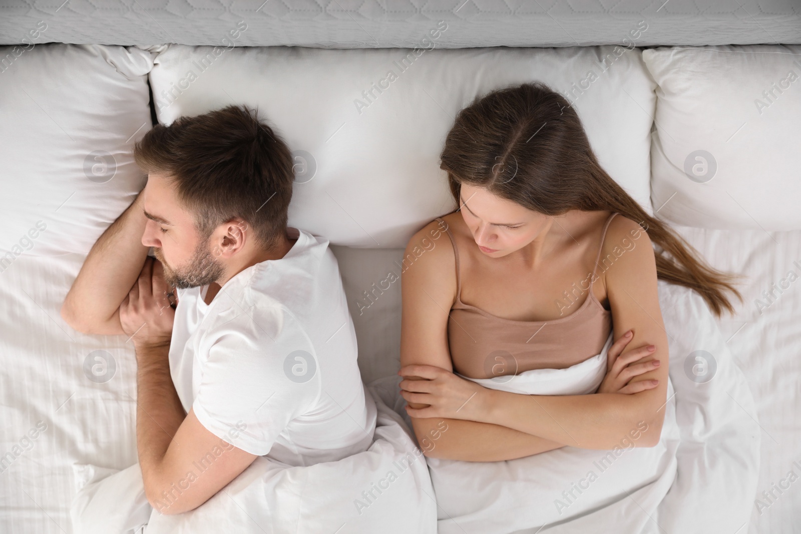 Photo of Upset young woman near sleeping husband in bed, top view. Relationship problems