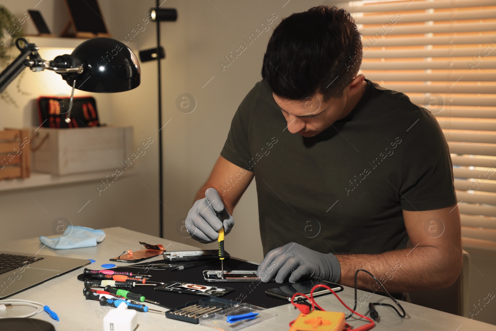 Photo of Technician repairing broken smartphone at table indoors