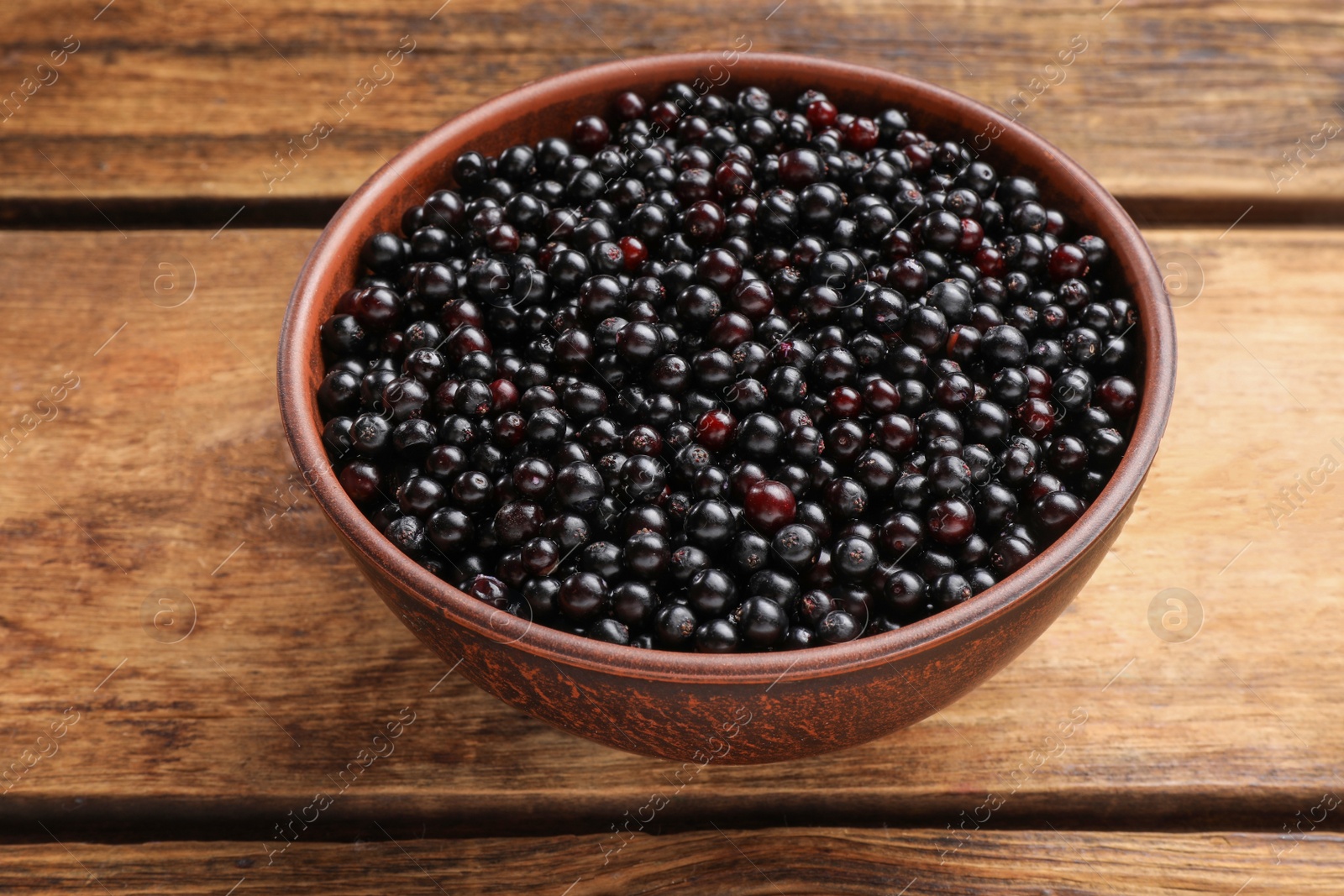 Photo of Bowl with elderberries (Sambucus) on wooden table, closeup