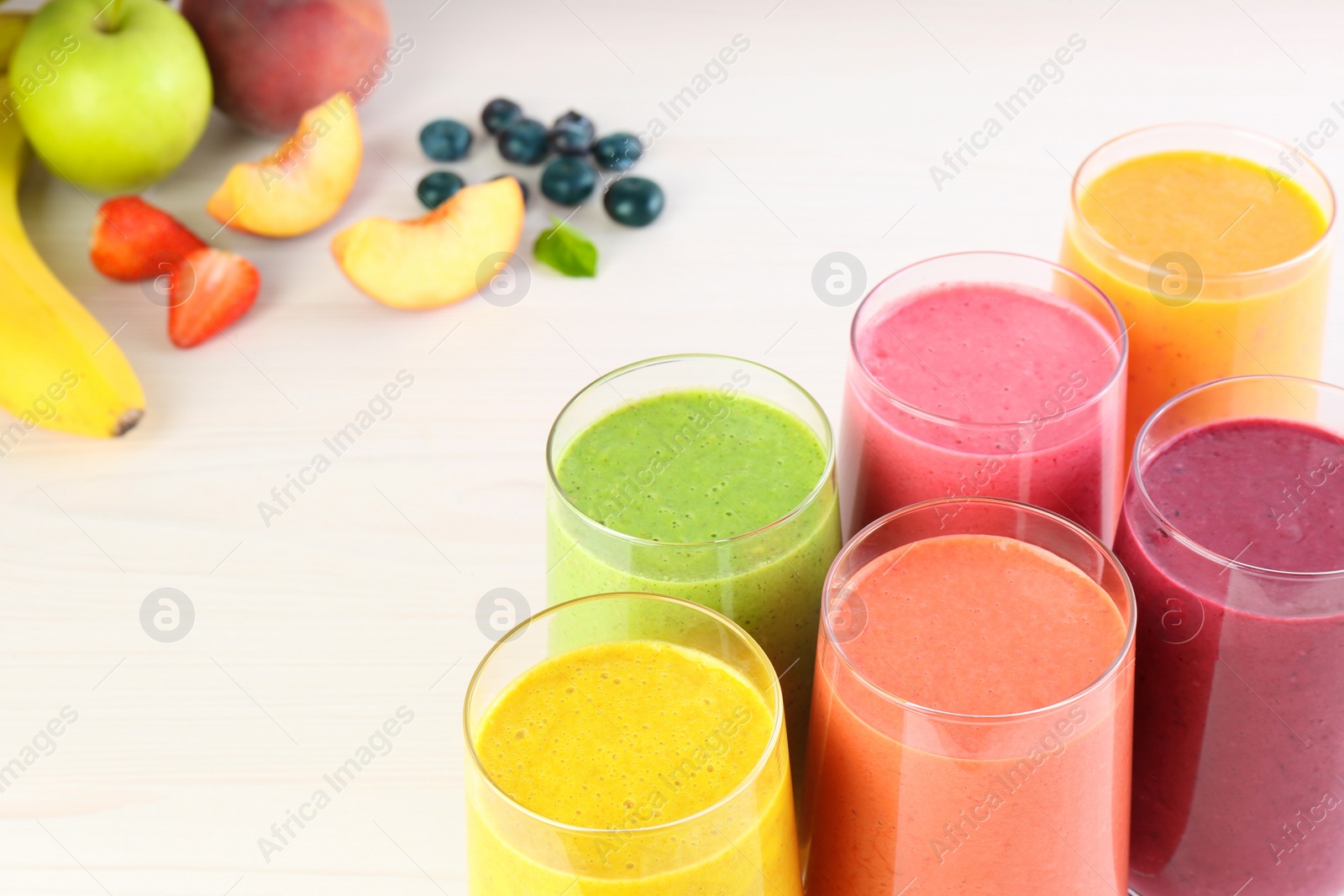 Photo of Fresh colorful fruit smoothies and ingredients on white wooden table