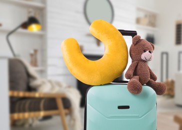 Image of Travel pillow and teddy bear on suitcase in room