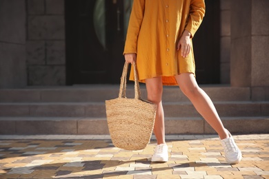 Photo of Woman in stylish yellow dress and sneakers with handbag on city street, closeup