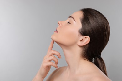 Young woman massaging her face on grey background. Space for text