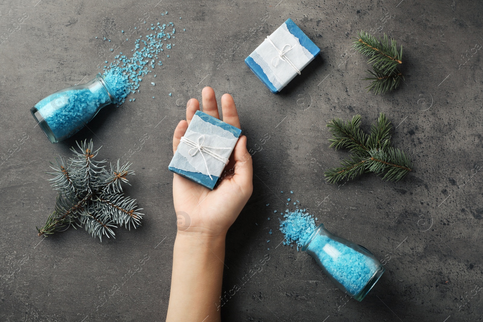 Photo of Woman holding handmade soap bar over table with ingredients, top view