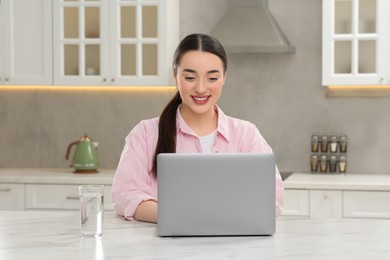 Photo of Woman using laptop at white table in kitchen