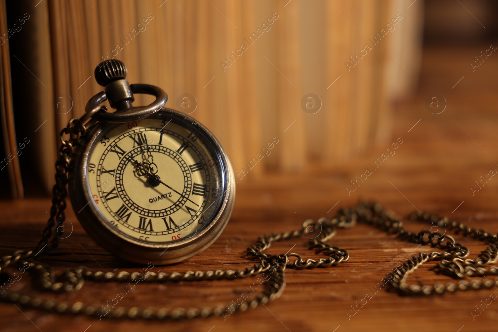 Photo of Pocket clock with chain on wooden table, closeup. Space for text
