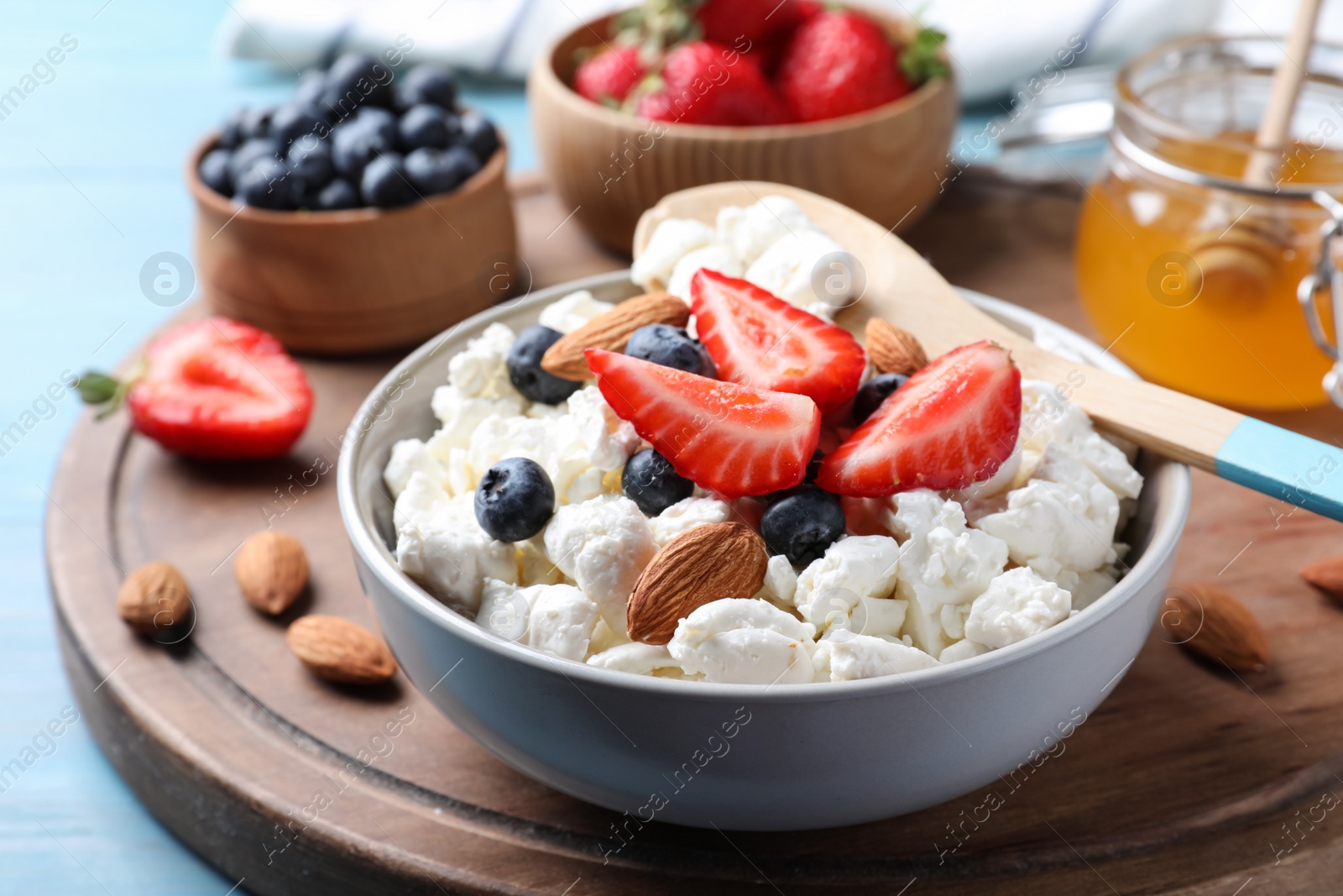 Photo of Bowl of fresh cottage cheese, berries and almonds on wooden board, closeup
