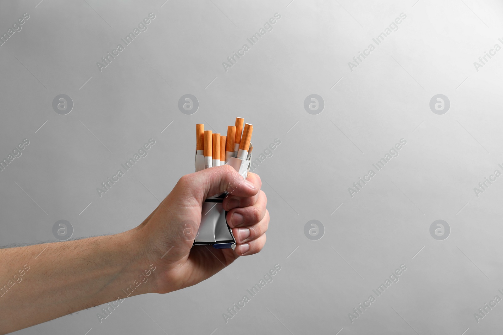 Photo of Stop smoking. Man holding pack with cigarettes on grey background, closeup. Space for text