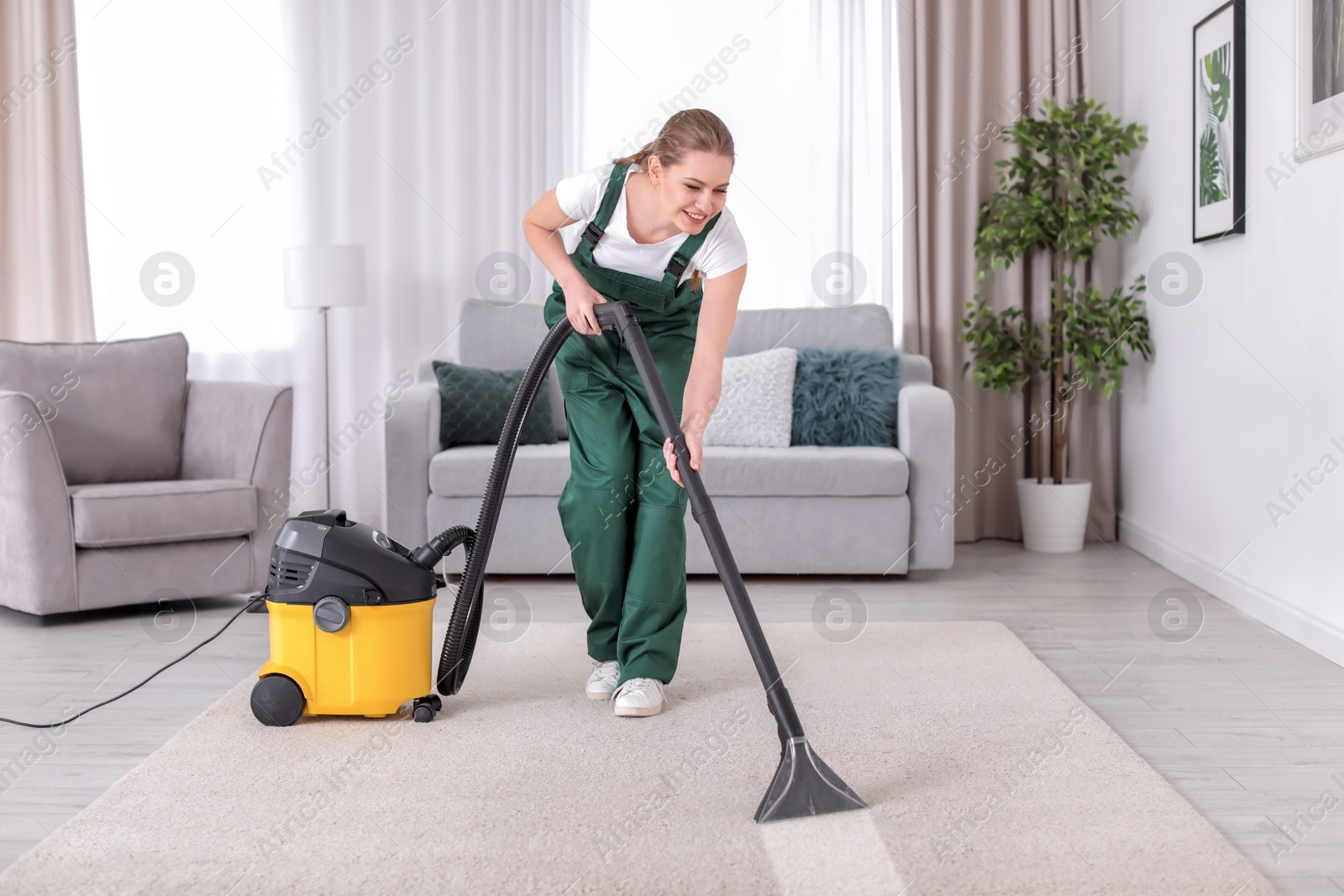 Photo of Female worker cleaning carpet with vacuum in living room