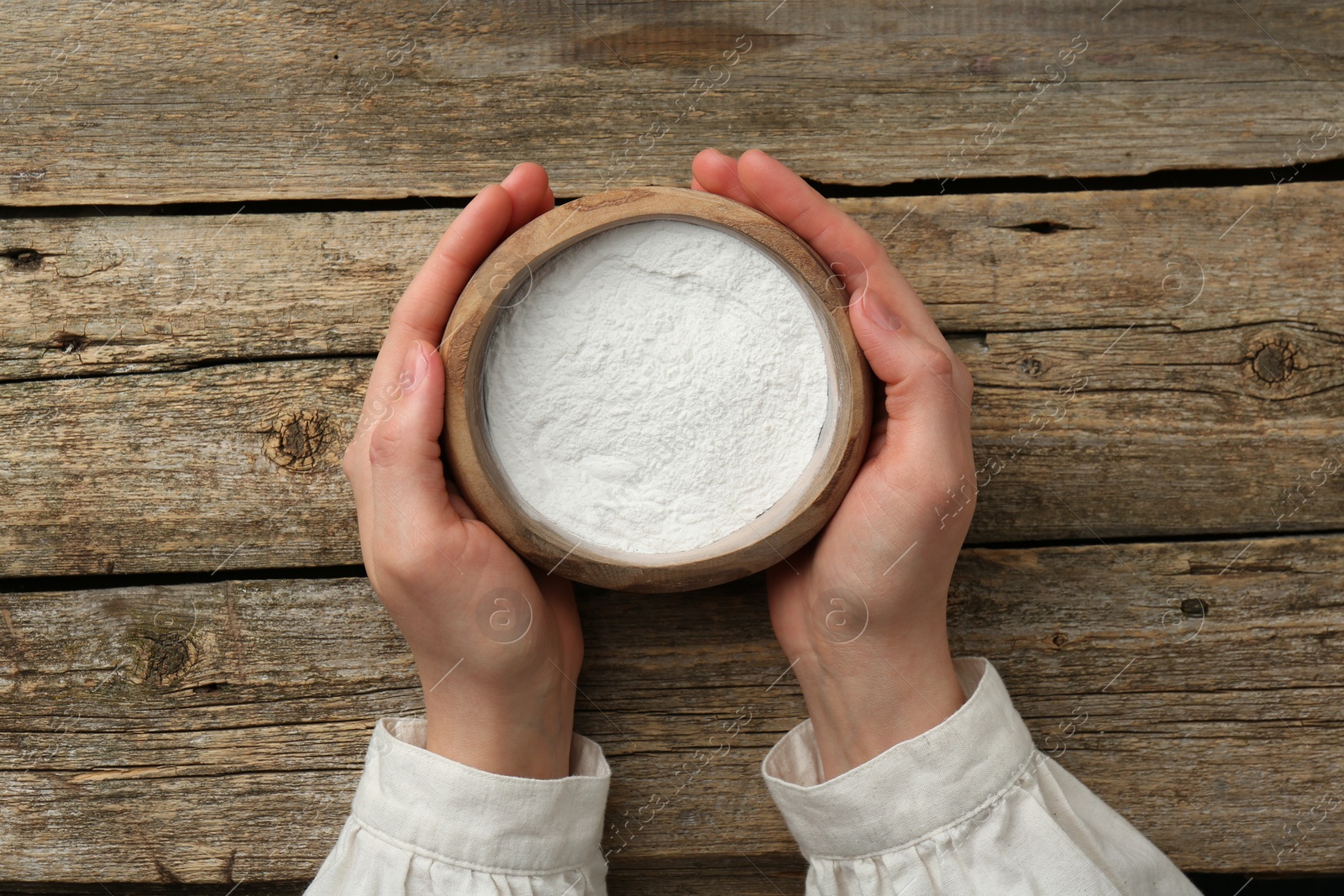 Photo of Woman holding bowl with baking powder at wooden table, top view