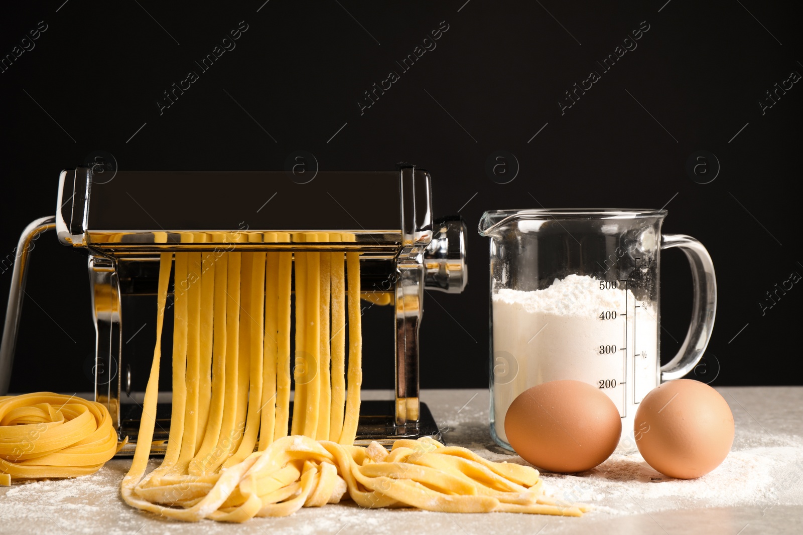 Photo of Pasta maker machine with dough and products on grey table against black background