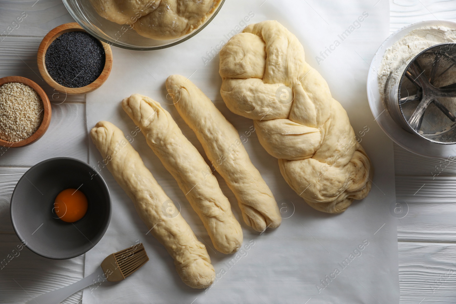 Photo of Homemade braided bread and ingredients on white wooden table, flat lay. Cooking traditional Shabbat challah