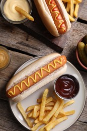 Delicious hot dogs, sauces and French fries on wooden table, flat lay