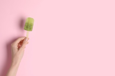 Photo of Woman holding delicious ice pop on pink background, closeup view with space for text. Fruit popsicle