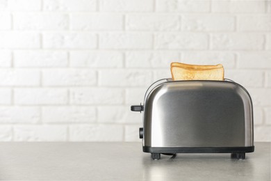 Photo of Electric toaster with bread slices on light table. Space for text