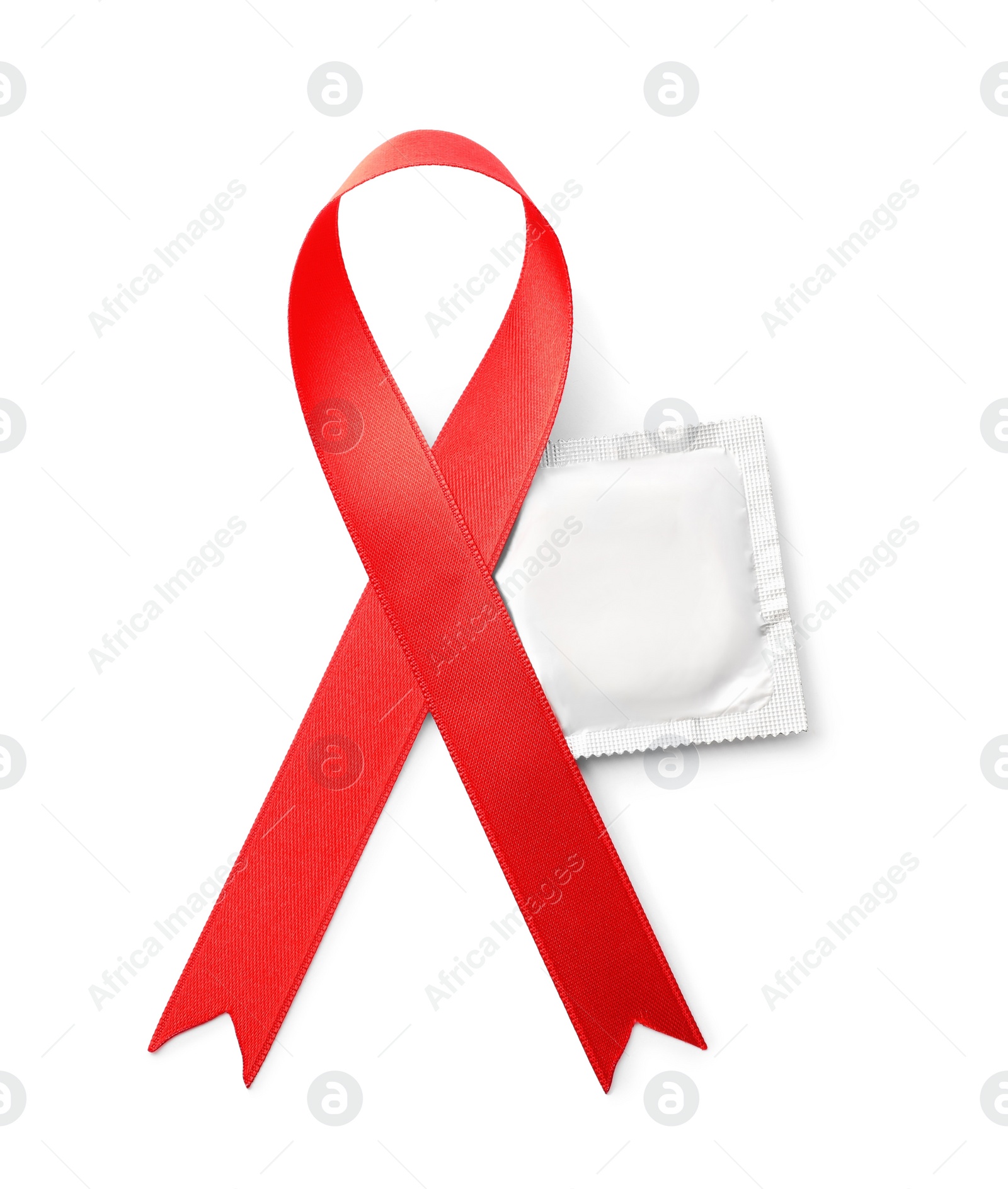 Photo of Red ribbon and condom isolated on white, top view. AIDS disease awareness