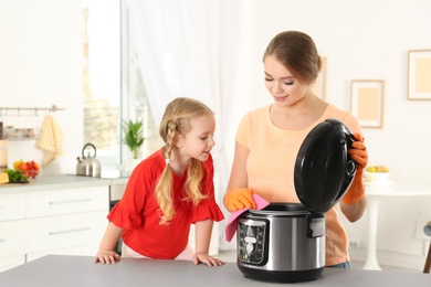 Mother and daughter cleaning modern multi cooker in kitchen
