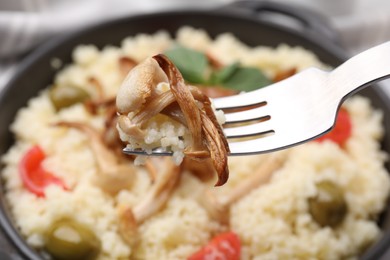 Photo of Fork with tasty couscous over frying pan, closeup