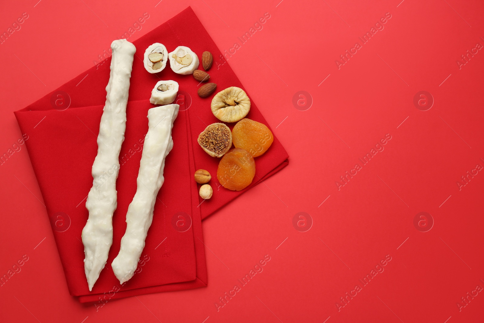 Photo of Delicious churchkhelas, nuts and dried fruits on red background, top view. Space for text