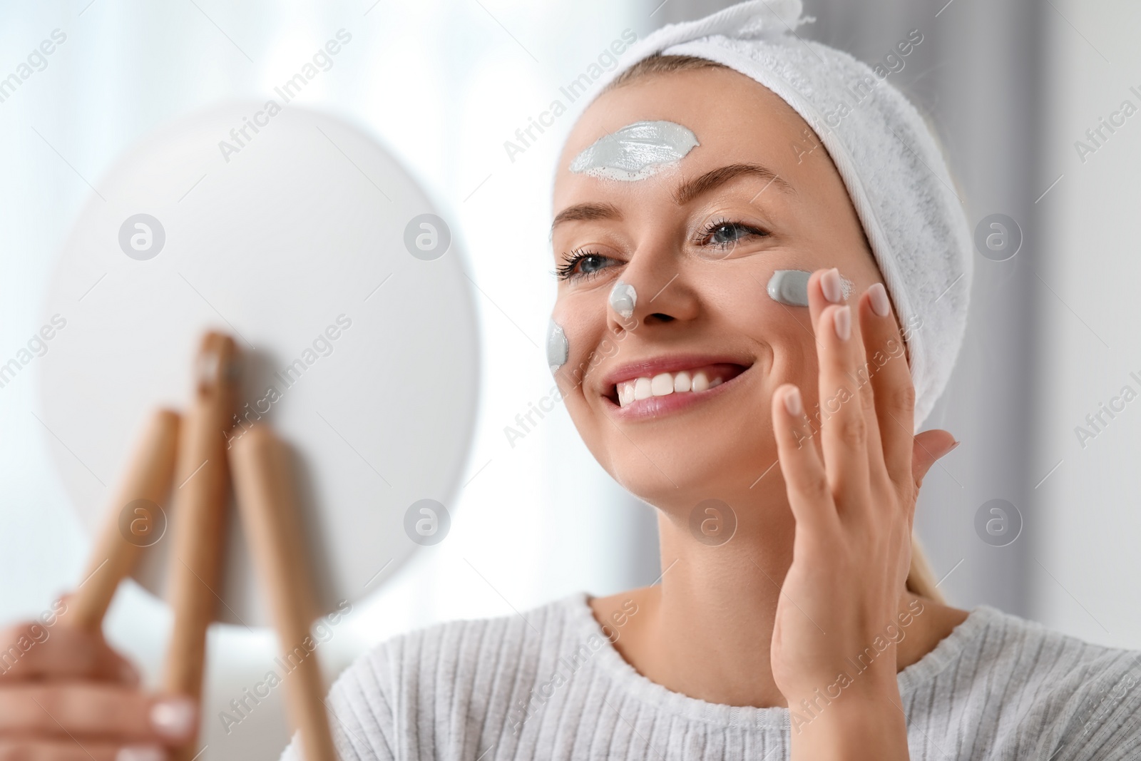 Photo of Young woman applying face mask in front of mirror indoors. Spa treatments
