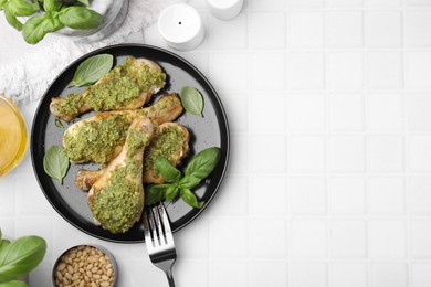 Delicious fried chicken drumsticks with pesto sauce, ingredients and fork on white tiled table, flat lay. Space for text