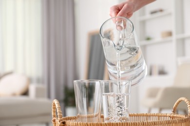 Photo of Woman pouring fresh water from jug into glass indoors, closeup. Space for text
