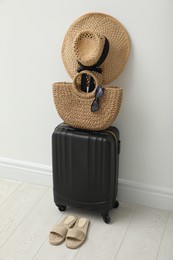Suitcase packed for trip, shoes and summer accessories near white wall indoors