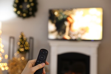 Photo of Woman with remote control in room decorated for Christmas, closeup