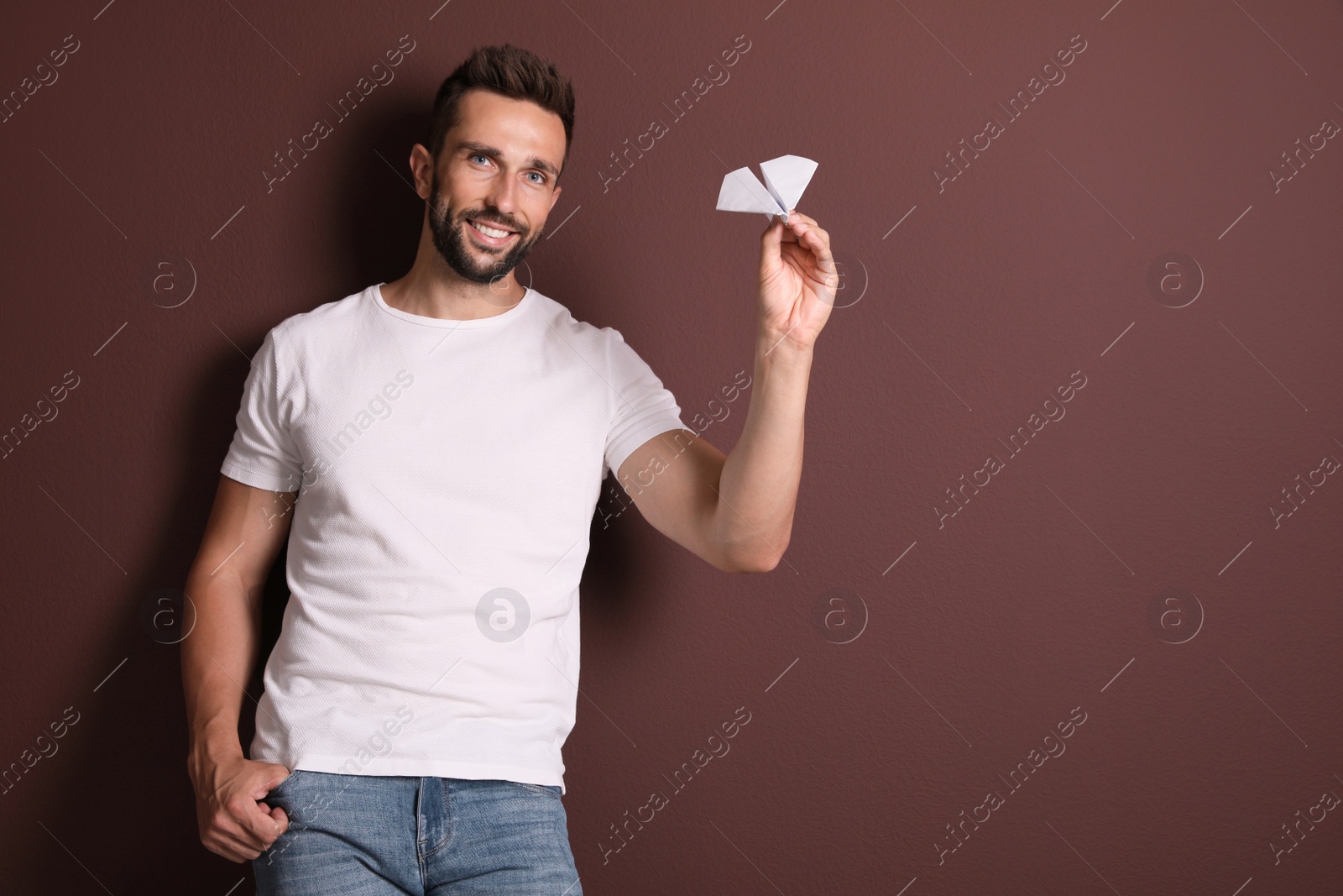 Photo of Handsome man playing with paper plane on brown background. Space for text