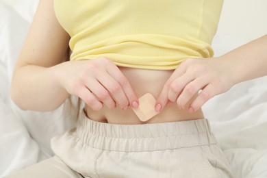 Woman applying contraceptive patch onto her belly on bed, closeup