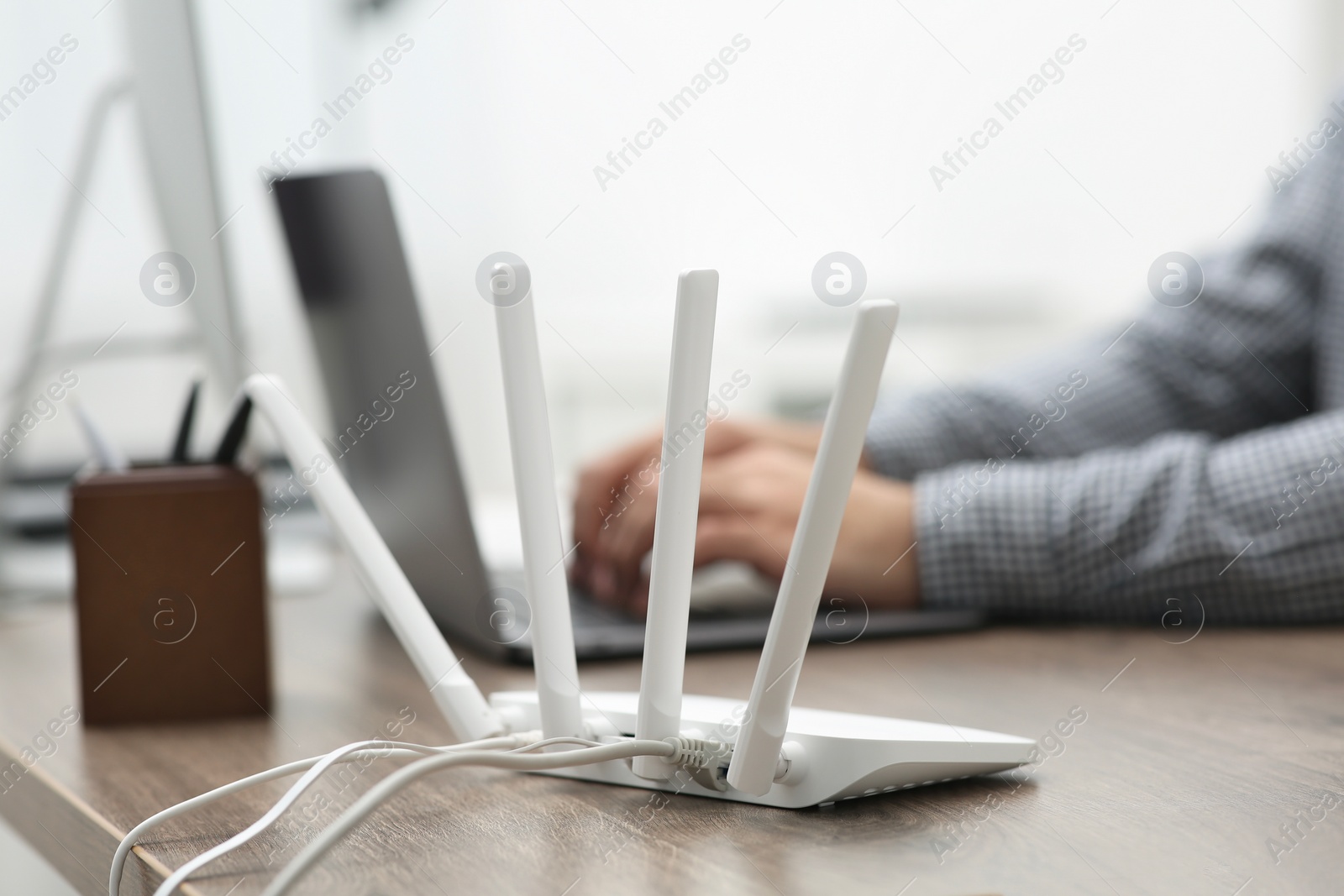 Photo of Man with laptop working at wooden table indoors, focus of Wi-Fi router