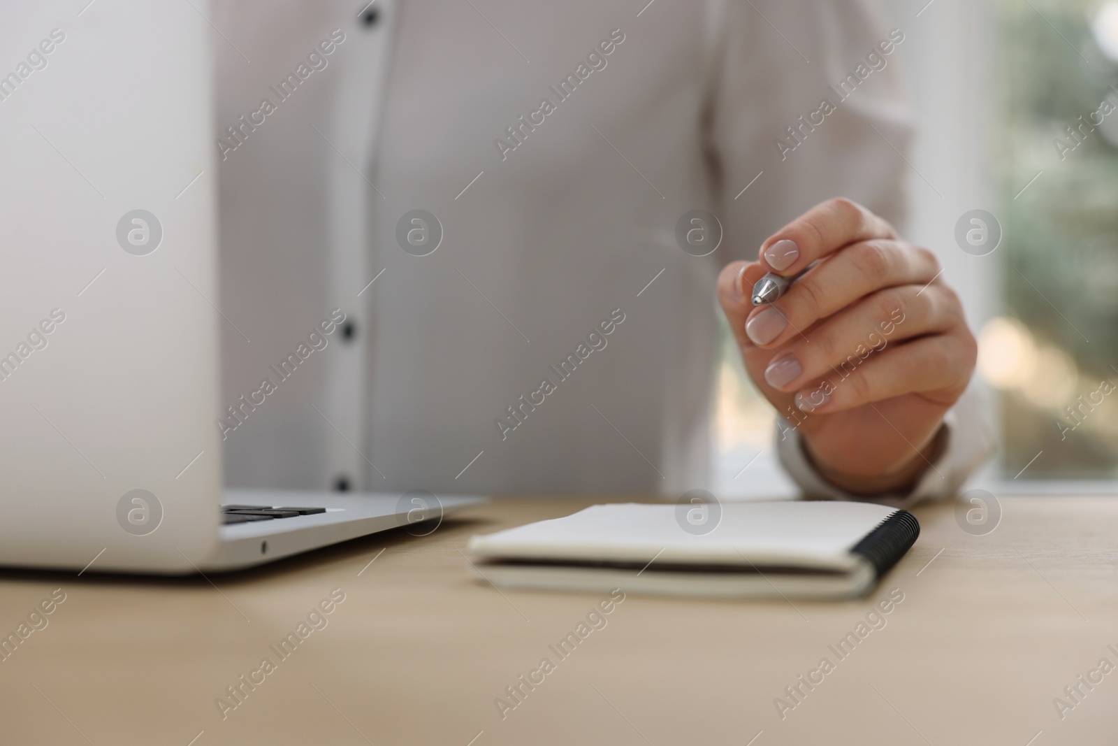 Photo of Woman with notebook and pen working on laptop at wooden table, closeup. Electronic document management