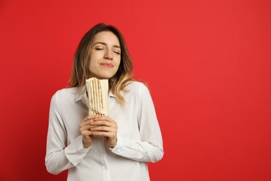 Young woman with delicious shawarma on red background, space for text
