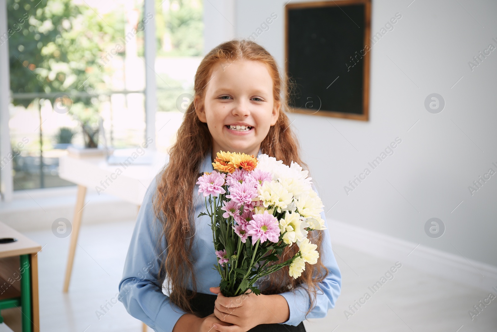 Photo of Happy schoolgirl with bouquet in classroom. Teacher's day