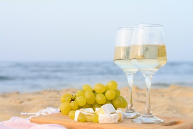 Photo of Glasses with white wine and snacks on sandy seashore. Space for text