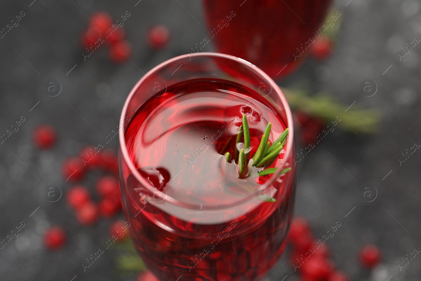 Photo of Tasty cranberry cocktail with rosemary in glass on gray table, closeup