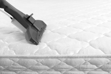 Photo of Using modern vacuum cleaner for mattress disinfection, closeup. Space for text