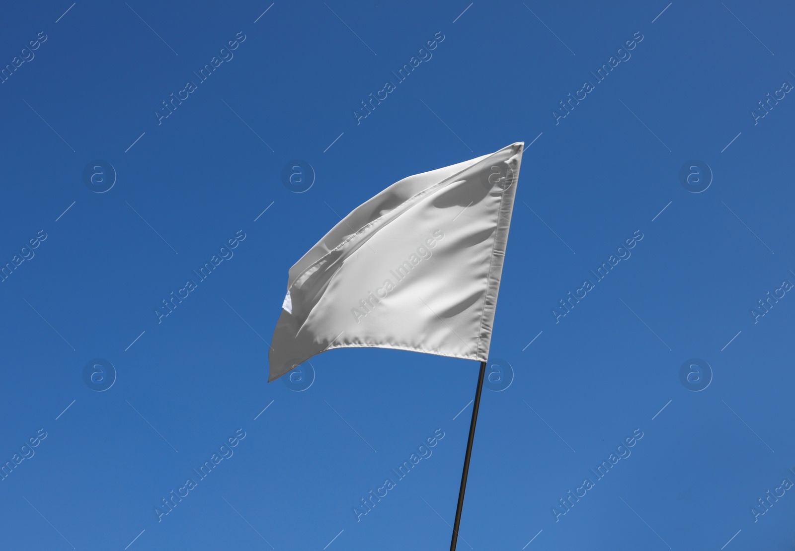 Photo of White flag fluttering against blue sky on sunny day