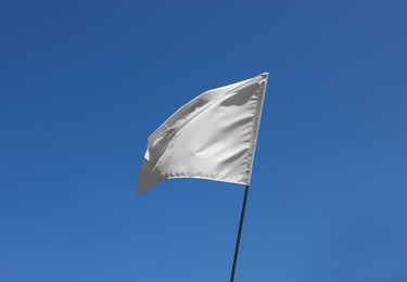 Photo of White flag fluttering against blue sky on sunny day