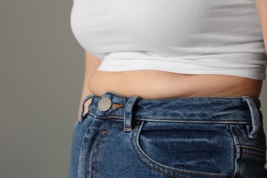 Photo of Overweight woman in tight tshirt and jeans on grey background, closeup