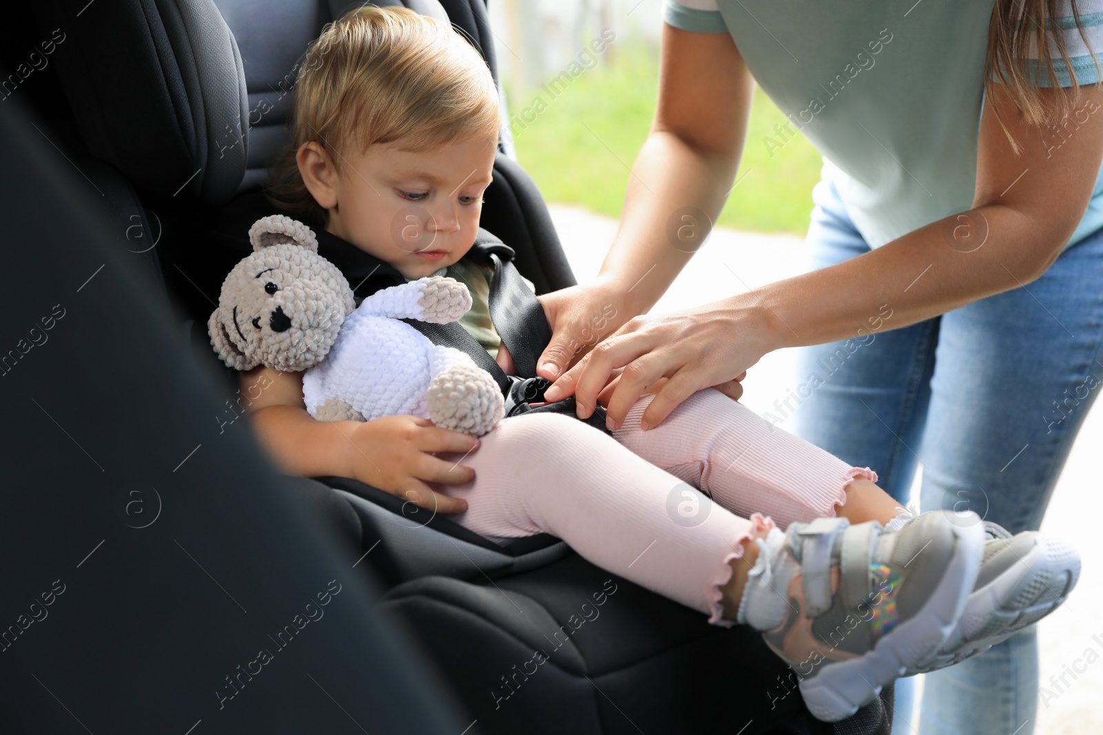 Photo of Mother fastening her daughter in child safety seat inside car