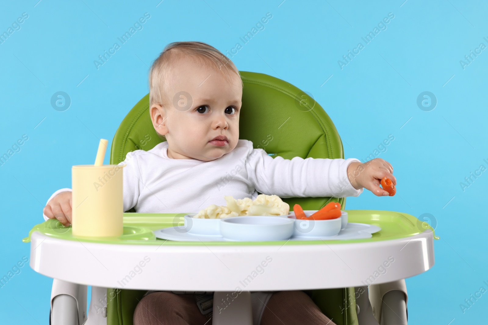 Photo of Cute little baby with healthy food in high chair on light blue background