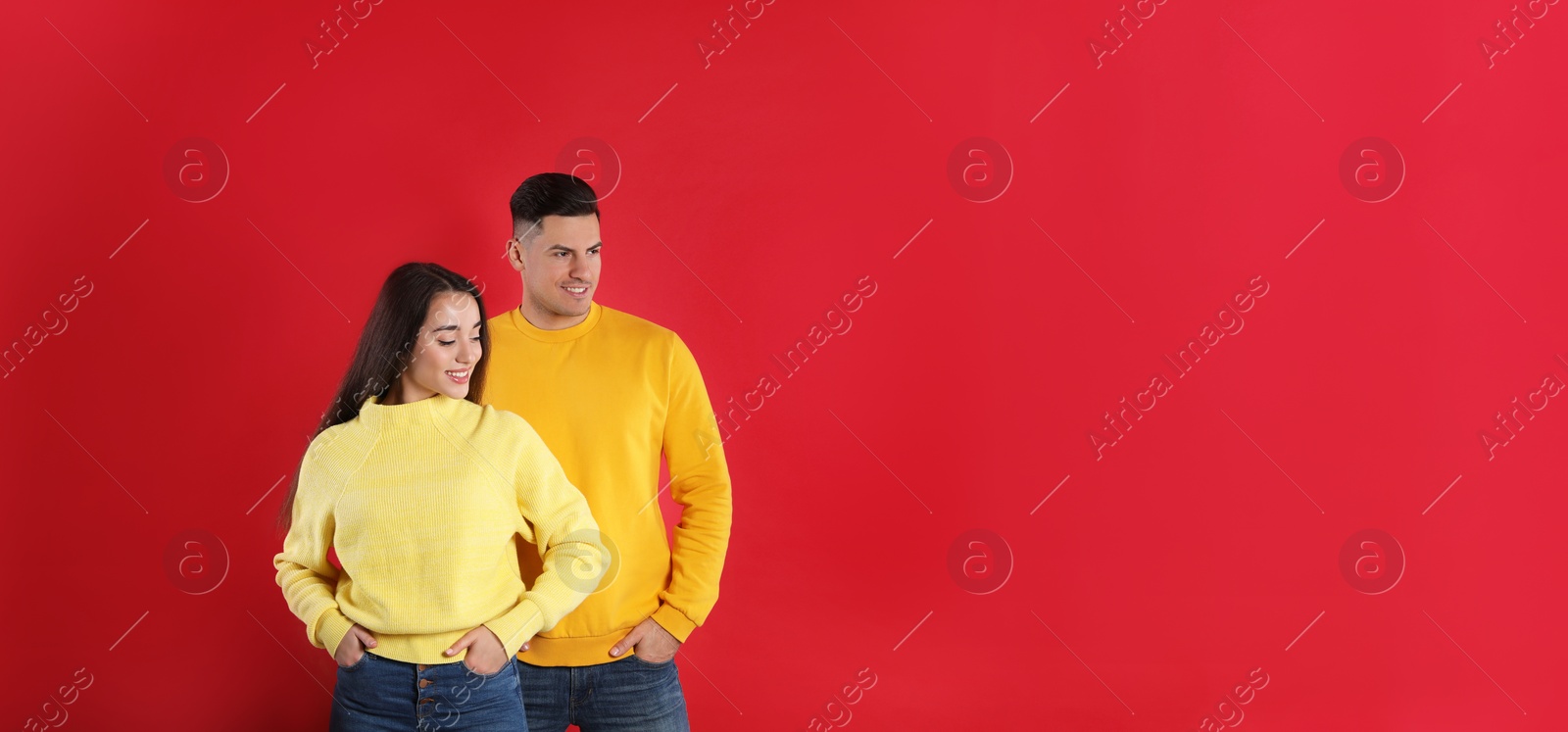 Photo of Happy couple wearing yellow warm sweaters on red background. Space for text