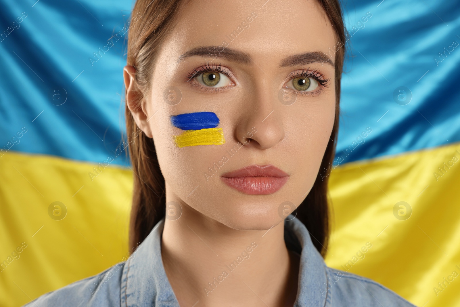 Photo of Young woman with face paint near Ukrainian flag, closeup