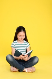 Photo of Cute little girl reading book on color background, space for text