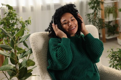 Photo of Relaxing atmosphere. Happy woman wearing headphones and listening music in room with beautiful houseplants